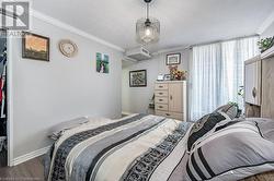 Bedroom with a wall mounted AC, wood-type flooring, a textured ceiling, and ornamental molding - 