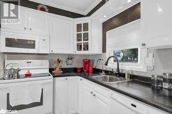 Kitchen featuring white appliances, white cabinetry, crown molding, and sink - 