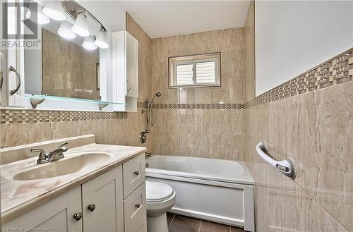 Full bathroom featuring vanity, tiled shower / bath combo, tile walls, tile patterned flooring, and toilet - 1476 Barton Street E, Hamilton, ON - Indoor Photo Showing Bathroom