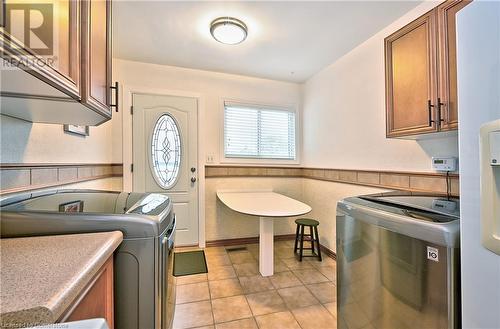 Clothes washing area with light tile patterned flooring, cabinets, and washing machine and clothes dryer - 1476 Barton Street E, Hamilton, ON - Indoor Photo Showing Laundry Room