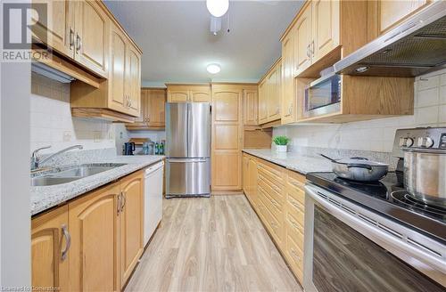 Kitchen featuring sink, appliances with stainless steel finishes, light hardwood / wood-style floors, light stone counters, and extractor fan - 375 King Street N Unit# 503, Waterloo, ON - Indoor Photo Showing Kitchen With Double Sink