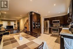 Kitchen with backsplash, appliances with stainless steel finishes, light tile patterned flooring, light stone counters, and dark brown cabinetry - 