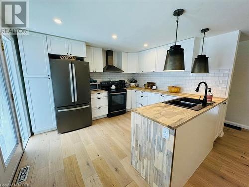 Kitchen featuring appliances with stainless steel finishes, sink, wall chimney range hood, pendant lighting, and white cabinetry - 541 Donald Street, Mattawa, ON - Indoor Photo Showing Kitchen With Double Sink