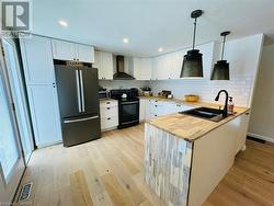 Kitchen featuring appliances with stainless steel finishes, sink, wall chimney range hood, pendant lighting, and white cabinetry - 