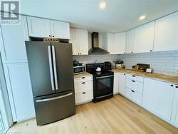 Kitchen featuring white cabinetry, stainless steel appliances, wall chimney range hood, and light hardwood / wood-style floors - 