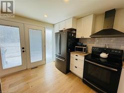 Kitchen with white cabinetry, french doors, stainless steel appliances, wall chimney range hood, and light hardwood / wood-style floors - 