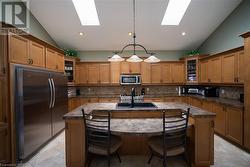 Kitchen with a center island with sink, decorative light fixtures, refrigerator, and lofted ceiling with skylight - 