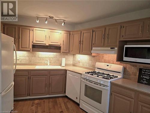 Kitchen with sink, dark wood-type flooring, track lighting, decorative backsplash, and appliances - 555 Main Street S Unit# 5, Callander, ON - Indoor Photo Showing Kitchen