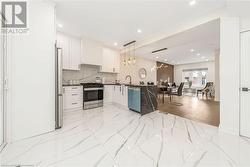 Kitchen featuring decorative light fixtures, stainless steel appliances, white cabinetry, and light hardwood / wood-style flooring - 