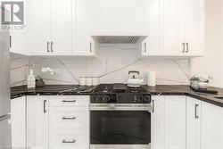 Kitchen featuring white cabinets, premium range hood, backsplash, and appliances with stainless steel finishes - 