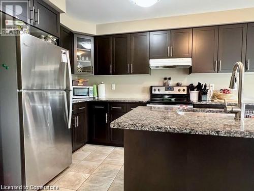 Kitchen featuring light stone countertops, appliances with stainless steel finishes, dark brown cabinetry, sink, and light tile patterned floors - 683 Robert Ferrie Drive, Kitchener, ON - Indoor Photo Showing Kitchen With Upgraded Kitchen