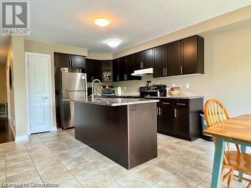 Kitchen with black electric range oven, a center island with sink, stainless steel fridge, light stone countertops, and dark brown cabinets - 683 Robert Ferrie Drive, Kitchener, ON - Indoor Photo Showing Kitchen