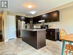 Kitchen with black electric range oven, a center island with sink, stainless steel fridge, light stone countertops, and dark brown cabinets - 