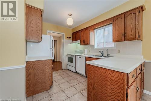 Kitchen with decorative backsplash, light tile patterned floors, white appliances, and sink - 10 Fenwick Court, Kitchener, ON 