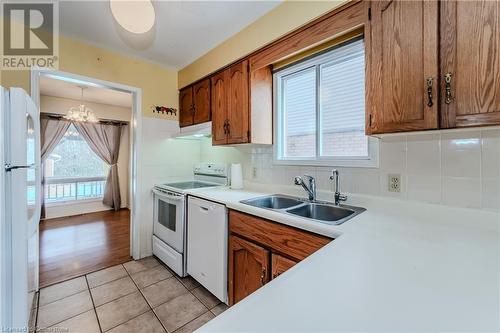 Kitchen featuring sink, an inviting chandelier, pendant lighting, white appliances, and light tile patterned floors - 10 Fenwick Court, Kitchener, ON 