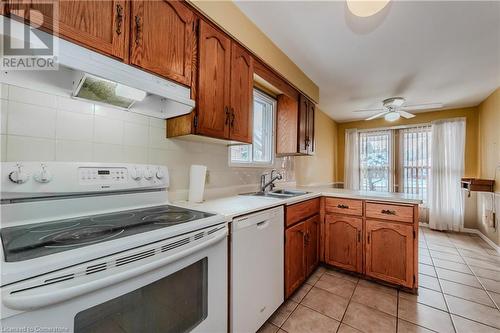 Kitchen with white appliances, backsplash, sink, light tile patterned flooring, and kitchen peninsula - 10 Fenwick Court, Kitchener, ON 