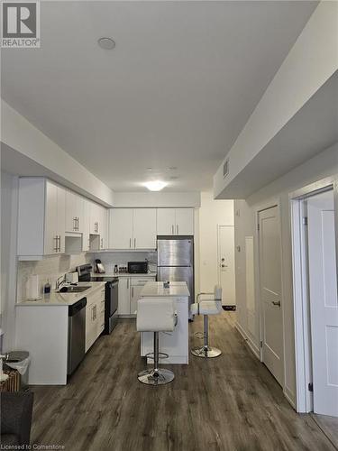 Kitchen featuring a kitchen bar, appliances with stainless steel finishes, dark hardwood / wood-style flooring, a center island, and white cabinetry - 251 Northfield Drive E Unit# 401, Waterloo, ON - Indoor Photo Showing Kitchen