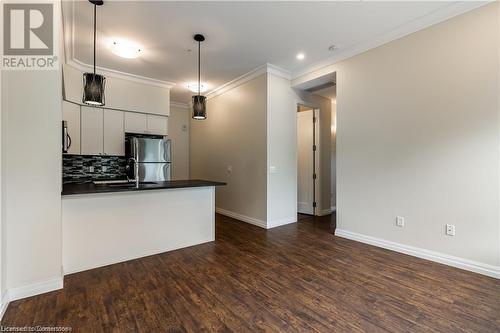 Kitchen with backsplash, dark wood-type flooring, hanging light fixtures, appliances with stainless steel finishes, and white cabinetry - 112 King Street E Unit# 305, Hamilton, ON - Indoor Photo Showing Kitchen