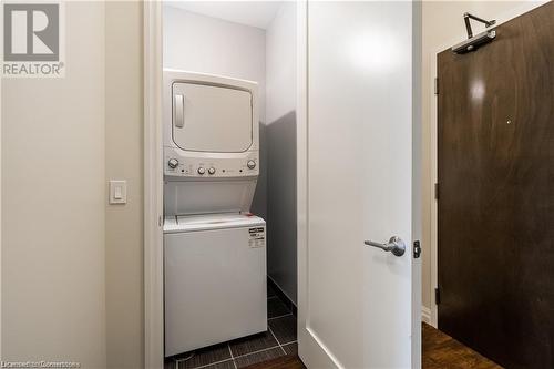 Clothes washing area with dark tile patterned flooring and stacked washing maching and dryer - 112 King Street E Unit# 305, Hamilton, ON - Indoor Photo Showing Laundry Room