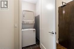 Clothes washing area with dark tile patterned flooring and stacked washing maching and dryer - 