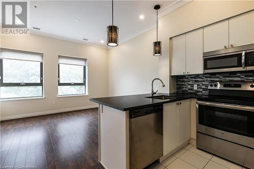 Kitchen with kitchen peninsula, light wood-type flooring, decorative light fixtures, white cabinetry, and stainless steel appliances - 112 King Street E Unit# 305, Hamilton, ON - Indoor Photo Showing Kitchen With Stainless Steel Kitchen