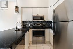 Kitchen featuring backsplash, sink, white cabinetry, and stainless steel appliances - 