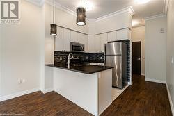 Kitchen featuring hanging light fixtures, stainless steel appliances, kitchen peninsula, wood-type flooring, and white cabinets - 