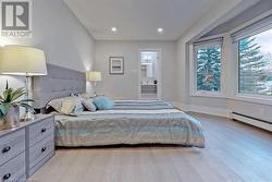 Bedroom featuring connected bathroom, a baseboard radiator, and light wood-type flooring - 