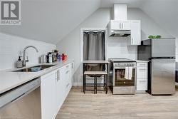 Kitchen with sink, light hardwood / wood-style flooring, vaulted ceiling, decorative backsplash, and appliances with stainless steel finishes - 