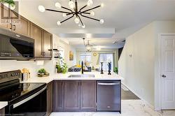 Kitchen featuring sink, stainless steel appliances, a notable chandelier, kitchen peninsula, and pendant lighting - 