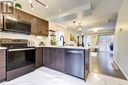 Kitchen with kitchen peninsula, a healthy amount of sunlight, stainless steel appliances, and an inviting chandelier - 