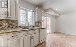 Kitchen with white dishwasher, white cabinets, sink, light stone countertops, and tasteful backsplash - 