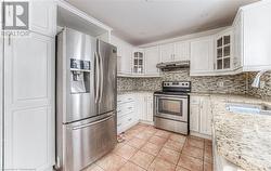 Kitchen with appliances with stainless steel finishes, light stone counters, sink, white cabinetry, and light tile patterned flooring - 