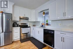 Kitchen with stainless steel appliances, sink, light hardwood / wood-style floors, white cabinetry, and hanging light fixtures - 