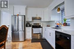 Kitchen with appliances with stainless steel finishes, sink, decorative light fixtures, light hardwood / wood-style flooring, and white cabinets - 