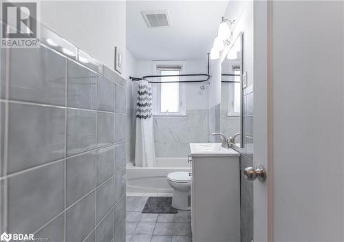 Full bathroom featuring tile patterned floors, shower / bath combination with curtain, toilet, vanity, and tile walls - 90 East 11Th Street, Hamilton, ON - Indoor Photo Showing Bathroom