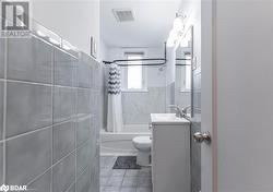 Full bathroom featuring tile patterned floors, shower / bath combination with curtain, toilet, vanity, and tile walls - 