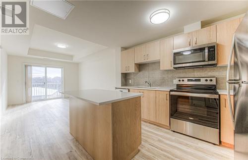 Kitchen featuring light brown cabinets, light hardwood / wood-style flooring, appliances with stainless steel finishes, tasteful backsplash, and a kitchen island - 301 Westmount Road W Unit# 204, Kitchener, ON - Indoor Photo Showing Kitchen