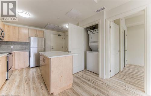 Kitchen with decorative backsplash, light wood-type flooring, stainless steel appliances, stacked washer and clothes dryer, and a kitchen island - 301 Westmount Road W Unit# 204, Kitchener, ON - Indoor Photo Showing Laundry Room