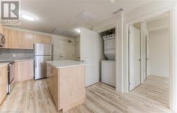 Kitchen with decorative backsplash, light wood-type flooring, stainless steel appliances, stacked washer and clothes dryer, and a kitchen island - 