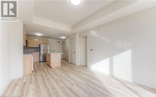 Kitchen with decorative backsplash, appliances with stainless steel finishes, a tray ceiling, a center island, and light hardwood / wood-style floors - 301 Westmount Road W Unit# 204, Kitchener, ON - Indoor Photo Showing Kitchen