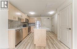 Kitchen with light wood-type flooring, light brown cabinets, a center island, and stainless steel appliances - 