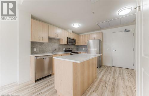 Kitchen featuring a center island, light brown cabinets, backsplash, light hardwood / wood-style floors, and appliances with stainless steel finishes - 301 Westmount Road W Unit# 204, Kitchener, ON - Indoor Photo Showing Kitchen