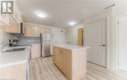 Kitchen featuring backsplash, sink, light hardwood / wood-style flooring, a kitchen island, and stainless steel refrigerator - 301 Westmount Road W Unit# 204, Kitchener, ON - Indoor Photo Showing Kitchen With Double Sink