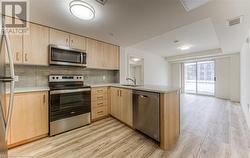 Kitchen with sink, light hardwood / wood-style flooring, light brown cabinetry, appliances with stainless steel finishes, and kitchen peninsula - 