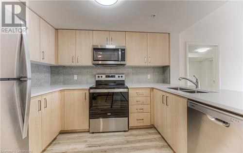 Kitchen with decorative backsplash, stainless steel appliances, sink, light brown cabinets, and light hardwood / wood-style flooring - 301 Westmount Road W Unit# G1, Kitchener, ON - Indoor Photo Showing Kitchen With Double Sink