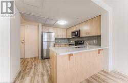 Kitchen featuring light hardwood / wood-style flooring, light brown cabinetry, appliances with stainless steel finishes, a kitchen bar, and kitchen peninsula - 