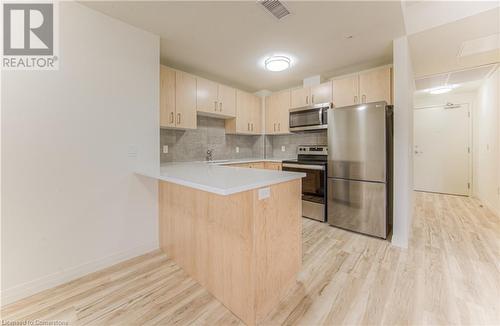 Kitchen featuring kitchen peninsula, light brown cabinets, light hardwood / wood-style flooring, and appliances with stainless steel finishes - 301 Westmount Road W Unit# 414, Kitchener, ON - Indoor Photo Showing Kitchen