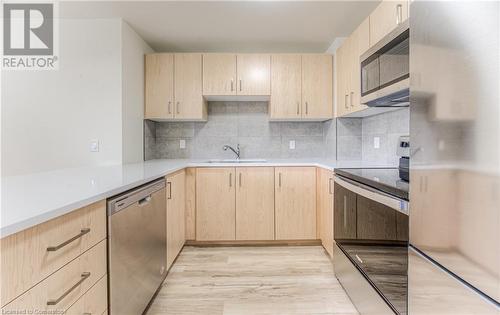 Kitchen featuring decorative backsplash, light brown cabinetry, light wood-type flooring, stainless steel appliances, and sink - 301 Westmount Road W Unit# 414, Kitchener, ON - Indoor Photo Showing Kitchen