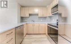 Kitchen featuring decorative backsplash, light brown cabinetry, light wood-type flooring, stainless steel appliances, and sink - 